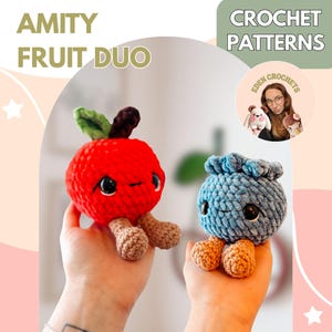 May include: The image features two crocheted fruit-shaped toys: a red apple and a blue blueberry. The apple has a green leaf and a brown stem, while the blueberry has a textured top. The toys have black eyes and tan legs. Text reads "AMITY FRUIT DUO" and "CROCHET PATTERNS".