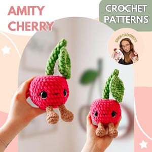 Könnte beinhalten: Zwei handgefertigte Häkelkirschen mit grünen Blättern und kleinen braunen Beinen werden gezeigt. Die Kirschen sind leuchtend rosa mit schwarzen Augen. Der Text "AMITY CHERRY" befindet sich oben links. Der Text "CROCHET PATTERNS" befindet sich oben rechts.