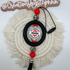 May include: A black silicone ring with a white charm that says "My Favorite People Call Me Mom" with red hearts. The ring is attached to a black tassel and a string of red and leopard print beads.