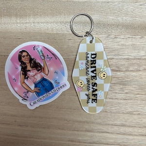 May include: A sticker and a keychain are displayed. The sticker features a cartoon woman with glasses, holding a drink, surrounded by butterflies. The keychain has a yellow and white checkered pattern with the text "DRIVE SAFE someone loves you."