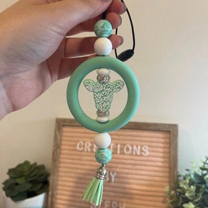 May include: A mint green silicone car charm with a white and green patterned cow design, white beads, and a mint green tassel.
