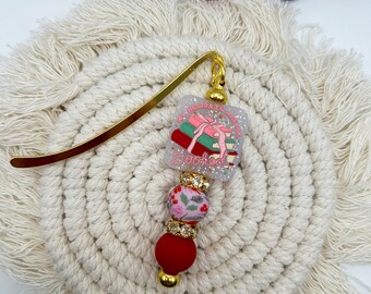 May include: Gold bookmark with a pink and green resin charm that says "My Holidays Are Booked". The charm is decorated with glitter and rhinestones. The bookmark also has a red bead and a white bead with a floral pattern.