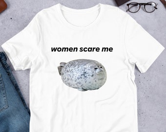 May include: White t-shirt with the text "women scare me" printed in black. A cartoon image of a seal is below the text.