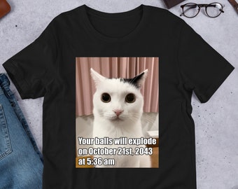 May include: Black t-shirt with a white cat looking at the camera. The text on the shirt reads "Your balls will explode on October 21st, 2043 at 5:36 am."