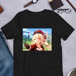 Könnte beinhalten: Schwarzes T-Shirt mit einem Cartoon-Bild eines Mädchens mit blonden Haaren, das einen roten Hut trägt und den Mittelfinger zeigt. Der Hintergrund ist eine Cartoon-Landschaft.