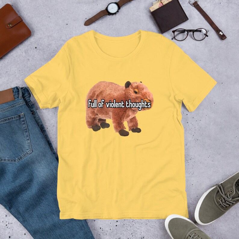 May include: Yellow short-sleeved t-shirt with a brown capybara plush toy and the text "Full of violent thoughts".