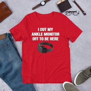May include: Red t-shirt with white text that reads "I cut my ankle monitor off to be here". A black ankle monitor is pictured below the text.