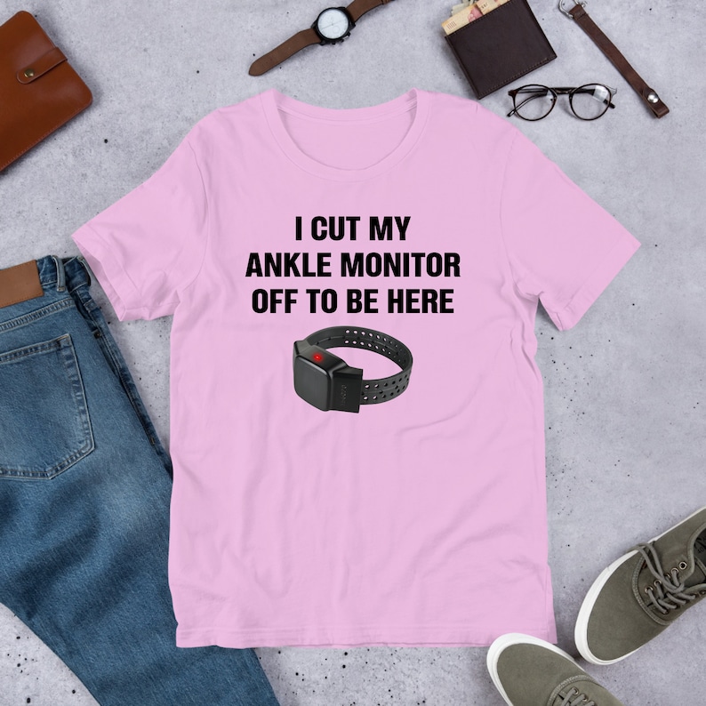 May include: Pink t-shirt with the text "I cut my ankle monitor off to be here" and a black ankle monitor with a red light on it.