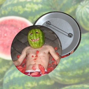 May include: A button featuring a man wearing a watermelon on his head, lying on a surface covered in watermelon pieces. The button is silver with a safety pin.