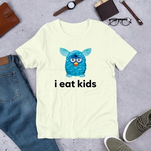 May include: A light yellow t-shirt with a blue fuzzy creature with big eyes and the text "i eat kids" printed on it.