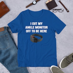 May include: A royal blue t-shirt with white text that reads "I cut my ankle monitor off to be here". A black ankle monitor with a red light is pictured below the text.
