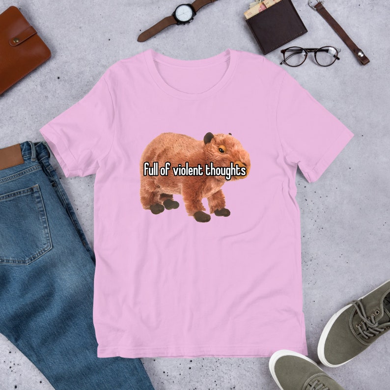 May include: Pink short-sleeved t-shirt with a brown capybara wearing a white shirt with the text "full of violent thoughts" printed on it.