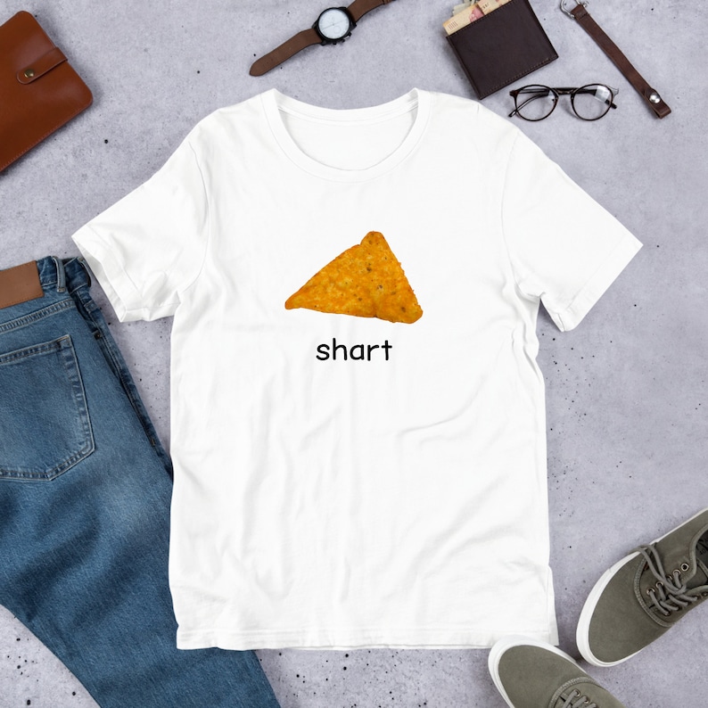 May include: White t-shirt with a picture of a tortilla chip and the word "shart" printed on it.