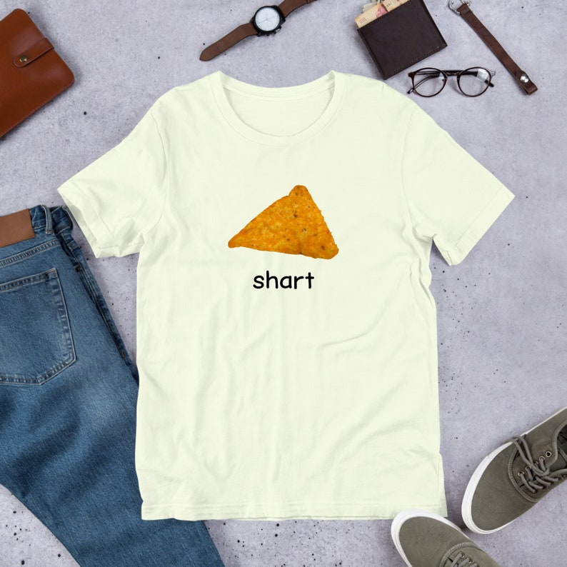 May include: A light yellow t-shirt with a picture of a nacho chip and the word "shart" printed on it.