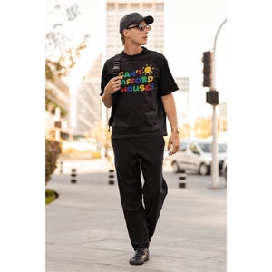 May include: A black t-shirt with a colorful graphic that says "Can't Afford House!" with a sun graphic above the text.