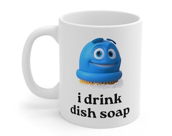 May include: White ceramic mug featuring a blue cartoon character with a smiling face and a sponge on its head. The text "i drink dish soap" is printed on the mug.