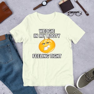 May include: A light yellow t-shirt with a cartoon smiley face and the text "WEDGIE IN MY BOOTY FEELING TIGHT".