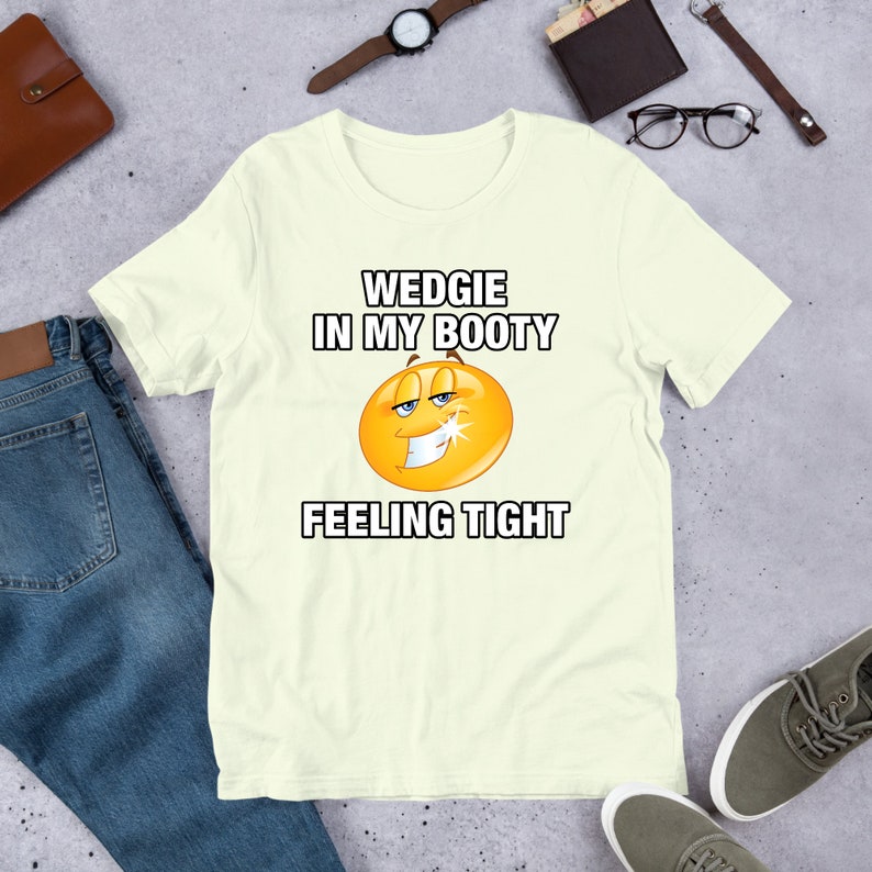 May include: A light yellow t-shirt with a cartoon smiley face and the text "WEDGIE IN MY BOOTY FEELING TIGHT".