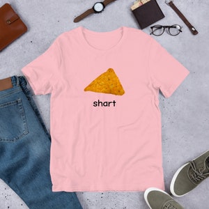 May include: A pink t-shirt with a graphic of a tortilla chip and the word "shart" printed on it.