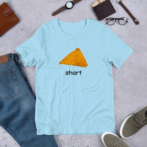 May include: A light blue t-shirt with a picture of a tortilla chip and the word "shart" printed on it.