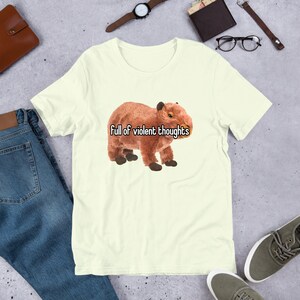 May include: A light yellow t-shirt with a brown capybara and the text "Full of violent thoughts" printed on the front.