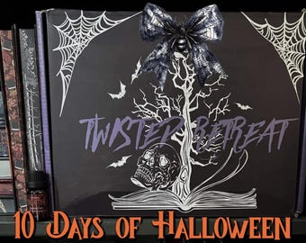 May include: A black rectangular box featuring a white graphic of a tree, a skull, an open book, spiderwebs, and bats. The text "TWISTED RETREAT" is printed in the center, and a black spider-themed bow is attached to the top. The text "10 DAYS OF HALLOWEEN" appears in orange at the bottom.