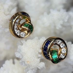 May include: A pair of gold earrings with a knot design. The earrings are set with diamonds, emeralds, and sapphires.