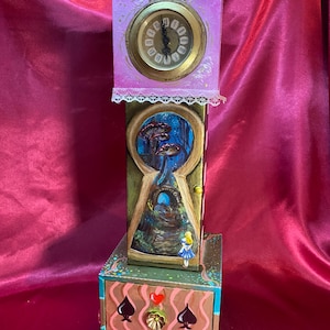 May include: A hand-painted clock with a pocket watch design. The clock features a keyhole scene with a mushroom forest and a girl in a blue dress. The drawer has spade, heart, and club symbols. The clock is a unique decorative item.