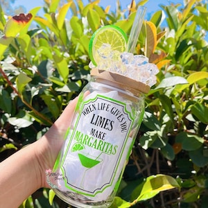 May include: A clear glass jar with a bamboo lid and a green and black label that reads "When life gives you limes make margaritas". The jar is filled with ice and a lime wedge. A glass straw is sticking out of the top of the jar.