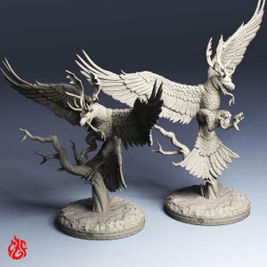 May include: Two unpainted light gray resin miniature figurines depicting mythical creatures with large feathered wings, deer-like antlers, and sharp talons. Each creature is perched on a textured tree branch base with a circular rocky foundation.