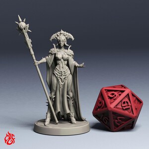 Könnte beinhalten: Eine graue, unbemalte Miniatur aus Kunstharz, die eine Fantasy-Figur in verzierter Rüstung mit langem Umhang zeigt, die einen hohen Stab mit einer stacheligen Kugel hält. Die Figur steht auf einem runden Sockel neben einem roten zwanzigseitigen Würfel.