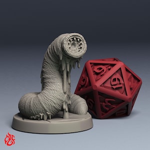 Puede incluir: Una figura gris con forma de gusano con una boca dentada detallada y una textura goteante, junto a un dado rojo de veinte caras. La figura está sobre una base circular y el dado tiene números visibles.