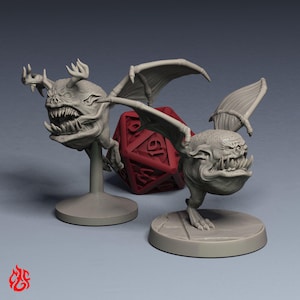 May include: Two gray, detailed fantasy creature figurines with large teeth and wings. One is mounted on a stand, the other on a circular base. A red twenty-sided die is between them. The figurines have horns and a menacing expression.