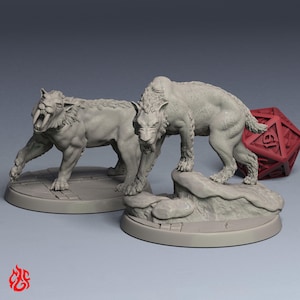 Può includere: Due miniature in resina grigia non dipinta raffiguranti gatti dai denti a sciabola in pose dinamiche, ciascuna montata su una base circolare con texture simile alla pietra. Un dado rosso a venti facce è posizionato dietro le figure.