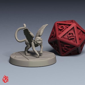 Op de afbeelding: Een grijze miniatuurfiguur van een gevleugeld aapachtig wezen, geposeerd op een cirkelvormige basis, met een rode twintigzijdige dobbelsteen. De aap heeft een grijnzende uitdrukking en gedetailleerde vleugels. De dobbelsteen is dieprood met witte cijfers.