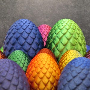 May include: A cluster of dragon eggs in various colours, including blue, green, pink, orange, and yellow. Each egg features a textured, scale-like pattern. The eggs are closely arranged, creating a vibrant and eye-catching display.