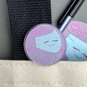 May include: A pink and blue round sticker with a cartoon face mask and the text "Please Wear a Mask".