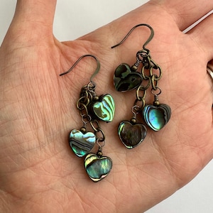 Pode incluir: Um par de brincos de argola com uma corrente e vários pingentes de coração de concha de abalone verde iridescente.