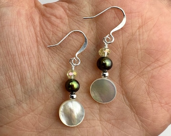 May include: A pair of drop earrings featuring silver-tone hooks, small faceted pale yellow beads, dark olive green spherical beads, and round, flat, iridescent white shell discs. The components are connected by silver-tone metal findings.