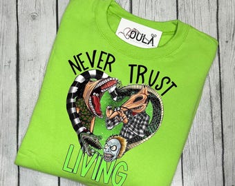 Puede incluir: Una sudadera de color verde lima con un estampado gráfico negro de tres personajes de la película "Pesadilla antes de Navidad". El texto "Never Trust The Living" está impreso en negro en la parte delantera de la sudadera.