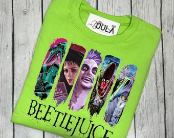 Puede incluir: Una camiseta verde con un estampado gráfico de personajes de la película "Beetlejuice". Los personajes están en blanco y negro con un fondo colorido. El texto "Beetlejuice" está impreso en negro debajo del gráfico.
