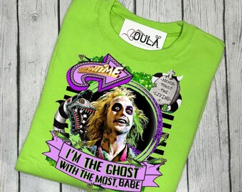 Puede incluir: Camiseta verde con un estampado gráfico de un personaje de la película Beetlejuice. El gráfico incluye el texto "I'm the ghost with the most, babe" y una lápida con el texto "Never trust the living."