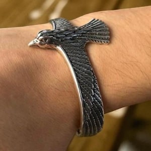 May include: A silver cuff bracelet with a detailed bird design. The bird's wings are spread, and the bracelet wraps around the wrist. The bird's head is at the top of the bracelet.