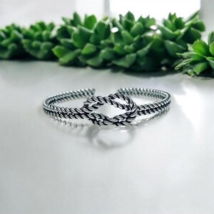 May include: A silver bracelet with a knotted design. The bracelet is made of twisted metal and has a polished finish.