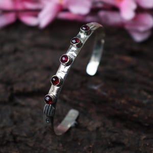 May include: A silver bangle bracelet with five red gemstones set into the band.