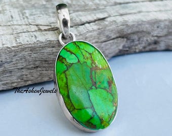 Puede incluir: Un colgante ovalado de turquesa verde con una argolla de plata. La turquesa tiene un patrón de mármol con vetas marrones.