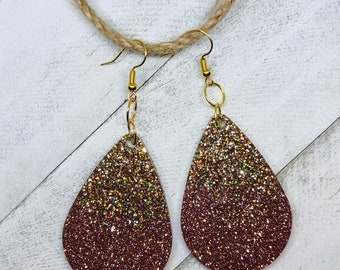 May include: A pair of teardrop-shaped earrings with a gold and rose gold glitter gradient. The earrings are made of a lightweight material and have a simple, elegant design.