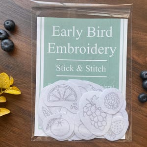Pode incluir: Um conjunto de 12 padrões de bordado brancos com diferentes frutas e vegetais. Os padrões são etiquetados como "Early Bird Embroidery Stick & Stitch".