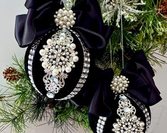May include: Two spherical black velvet ornaments decorated with silver-toned filigree, clear rhinestones, and white faux pearls. Each ornament features a large black satin ribbon bow at the top and vertical rows of silver rhinestone trim.