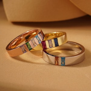 May include: Three rings with colorful rectangular gemstones. One ring is rose gold, one is gold, and one is silver. The gemstones are arranged in a vertical stripe pattern, showcasing a variety of colors including blue, green, and pink.